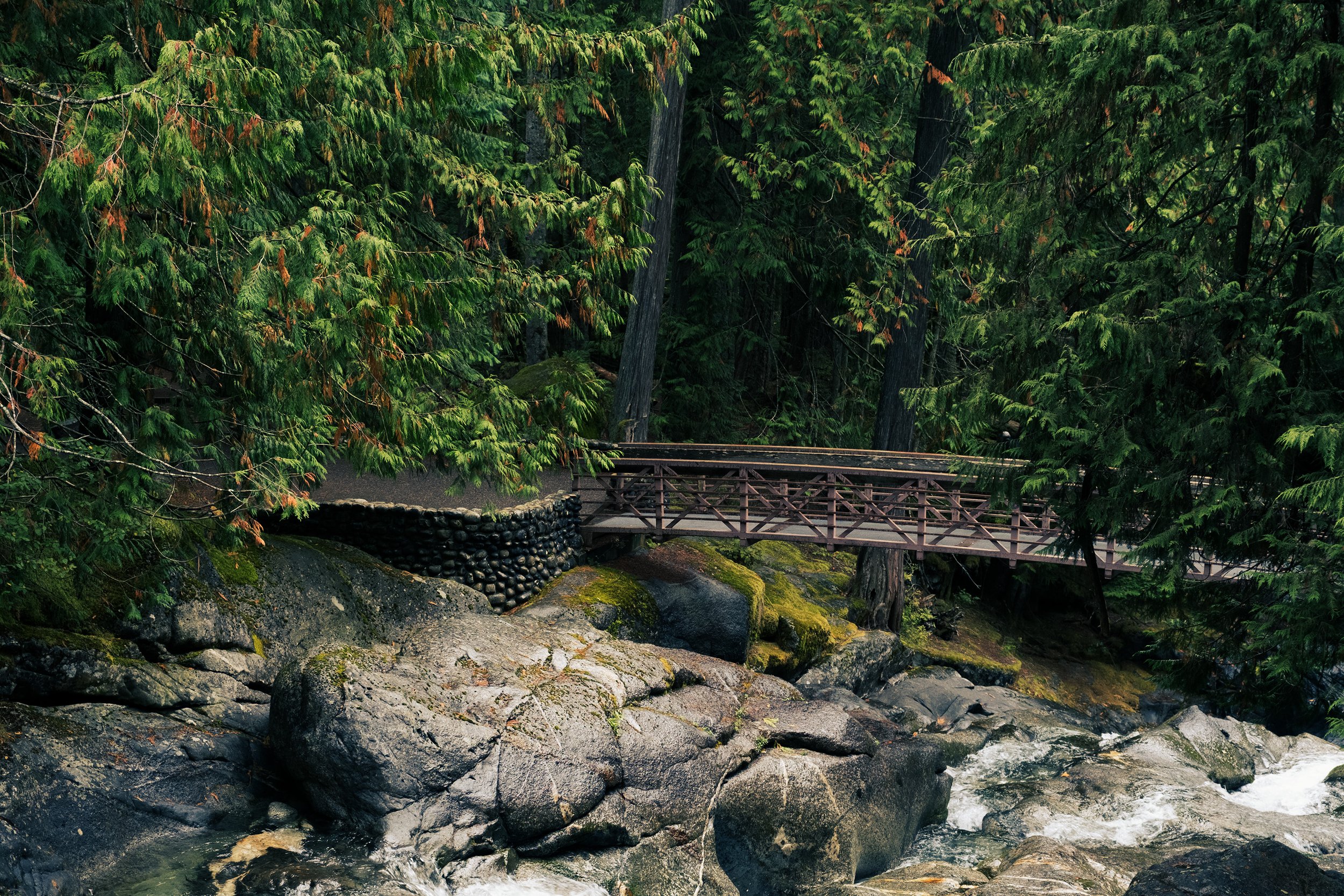 A timber footbridge crossing a rocky Pacific Northwest stream